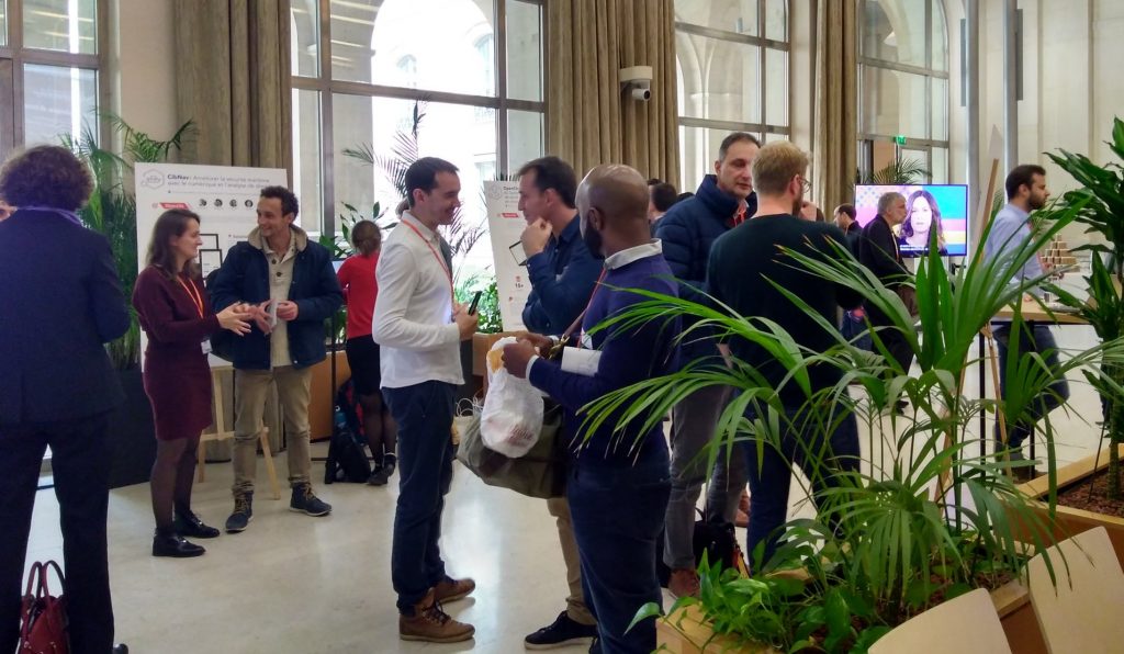 Des personnes discutent devant des stands de démonstration, dans une grande salle.